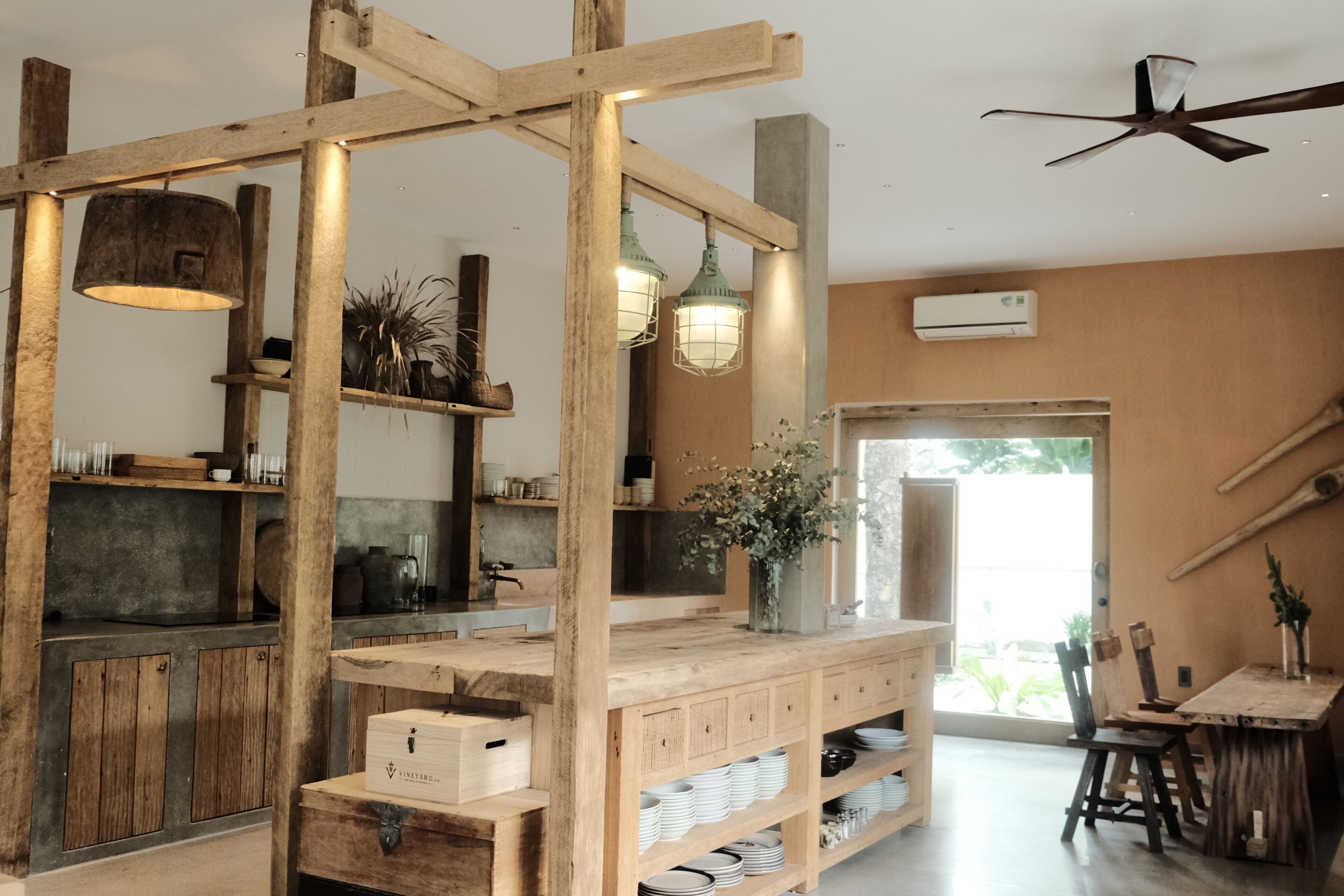 A rustic interior with exposed wooden beams, a central wooden structure with shelves, hanging lights, and a ceiling fan.