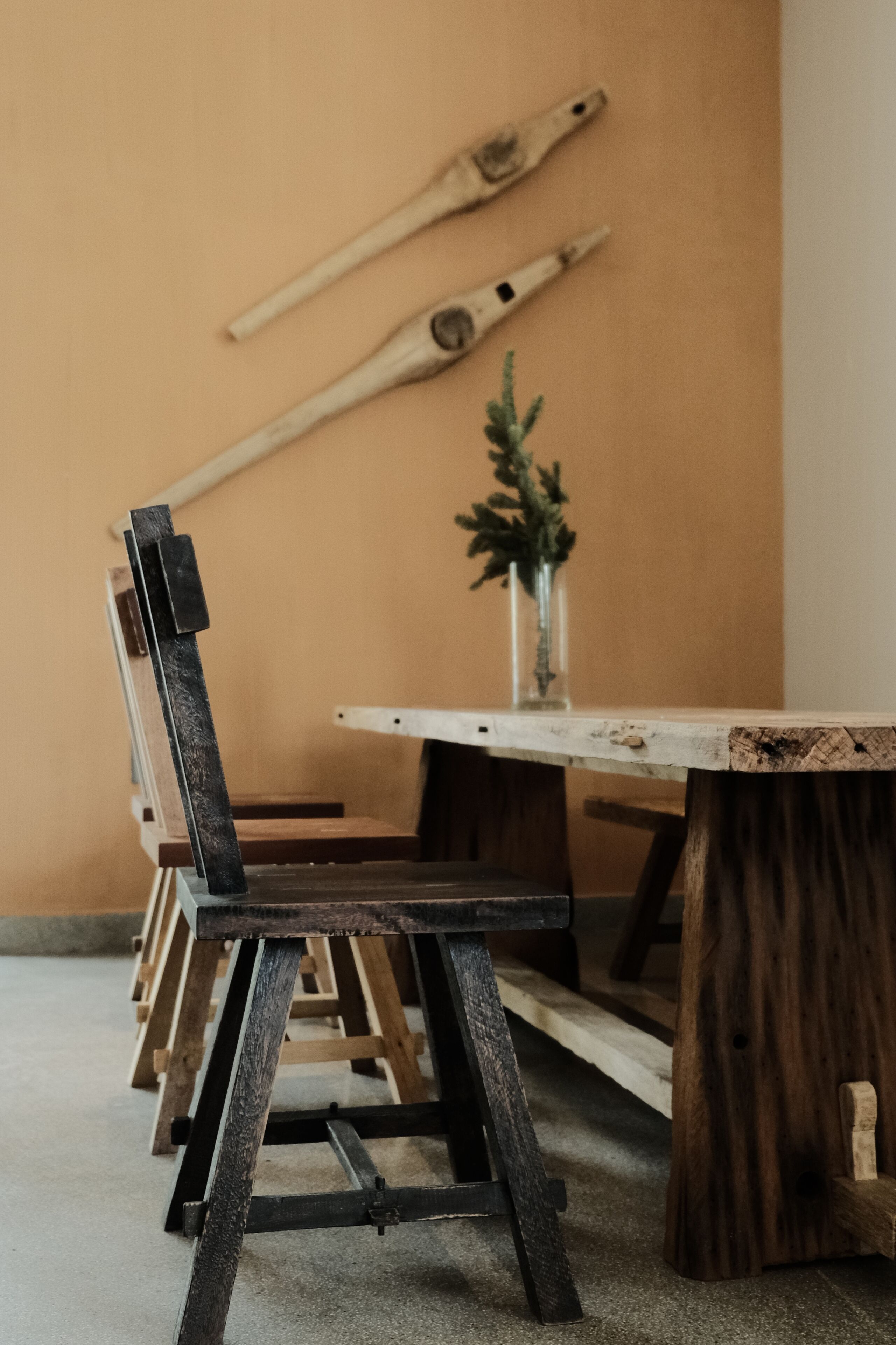A dining area with a wooden table and chairs, a small plant on the table, and a wall with two wooden bats.