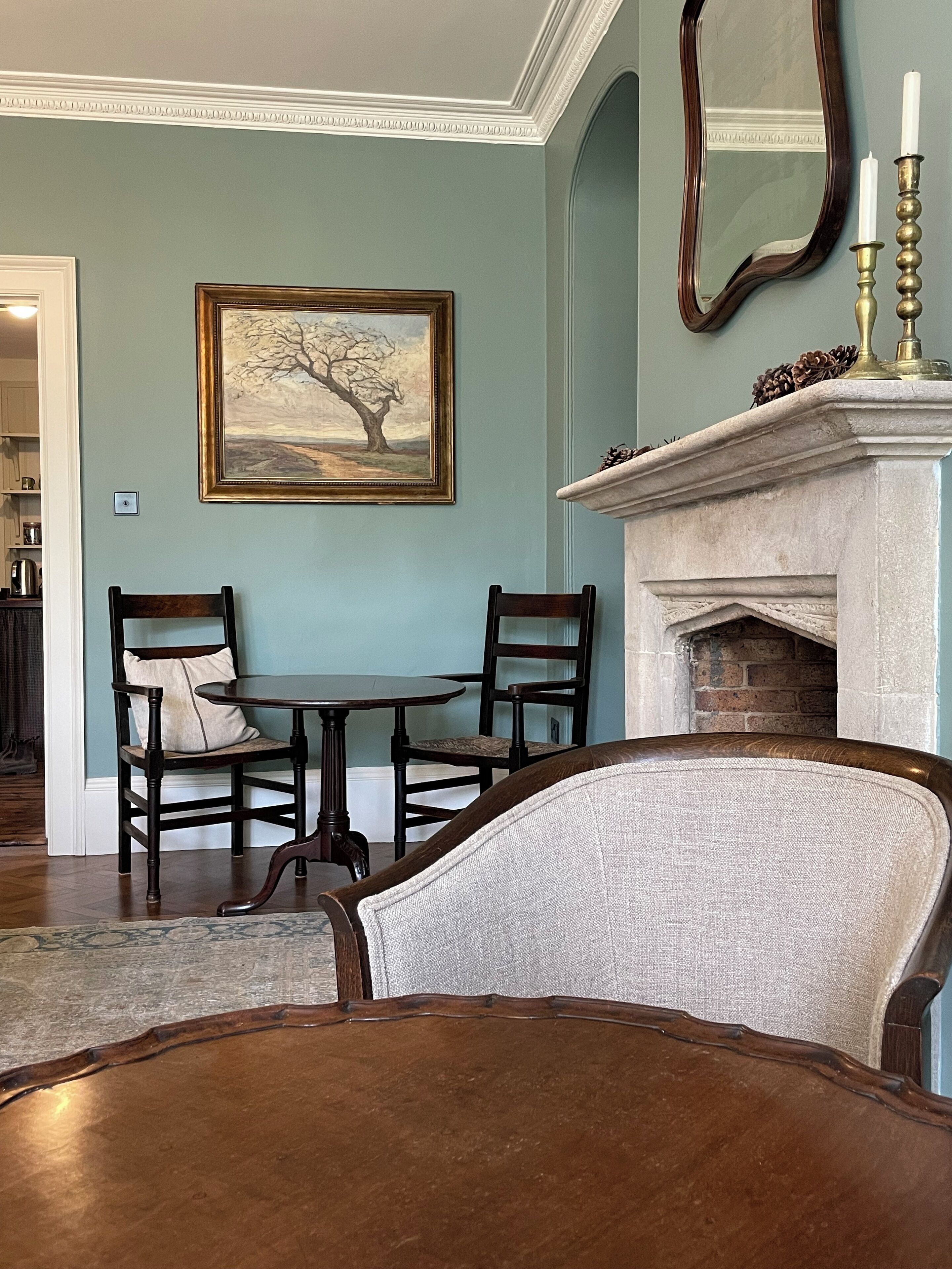 A living room with a fireplace, a painting, and two chairs.
