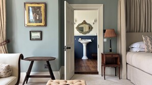 A bedroom with a bed, a bedside table, a lamp, a chair, a small table, and a mirror.