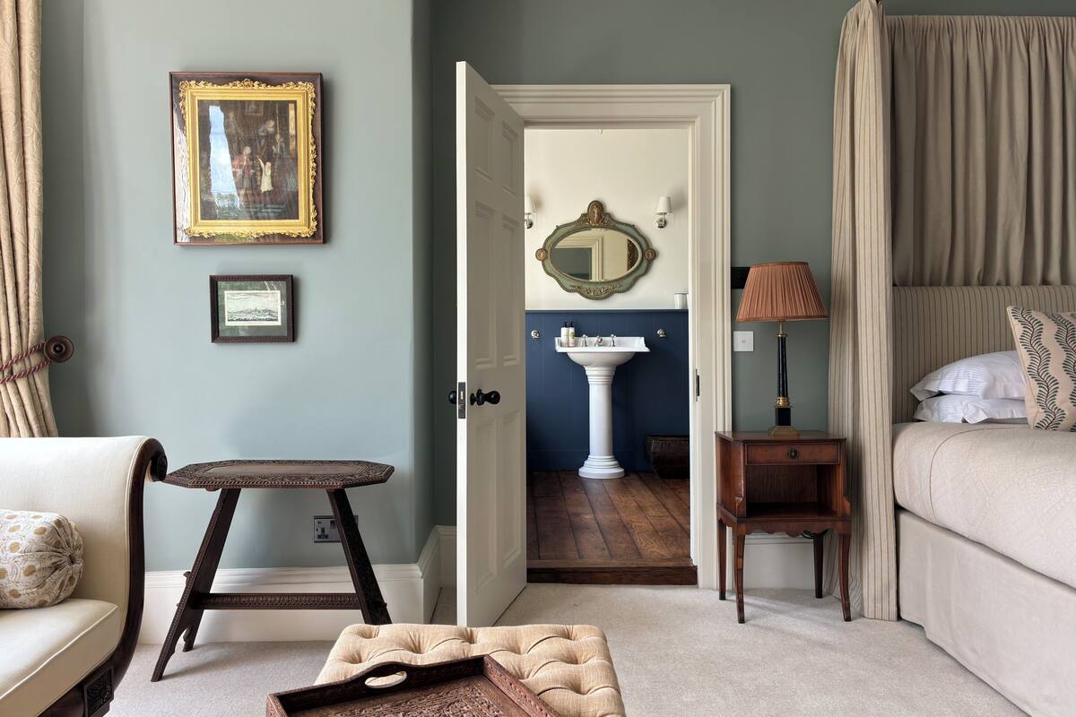 A bedroom with a bed, a bedside table, a lamp, a chair, a small table, and a mirror.