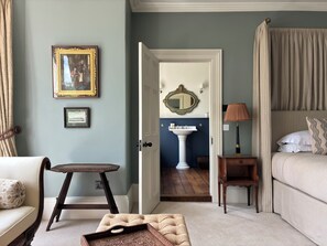 A bedroom with a bed, a bedside table, a lamp, a chair, a small table, and a mirror.