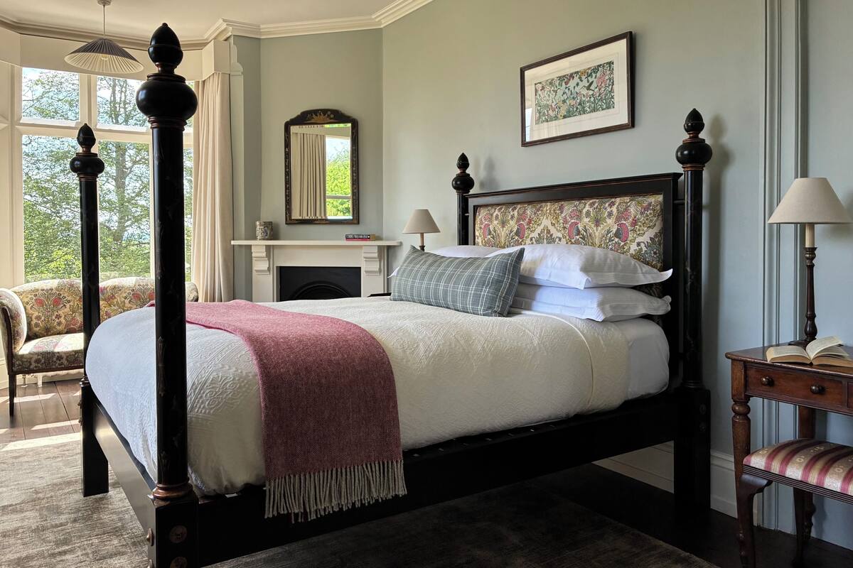 A four-poster bed with a fireplace, a mirror, and a framed floral artwork on the wall.
