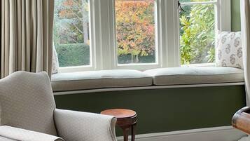 A room with a large window, a cushioned bench, a chair, and a small table.