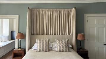 Un dormitorio con una cama grande, dosel, dos mesitas de noche con lámparas, ventana con vistas y una puerta.
