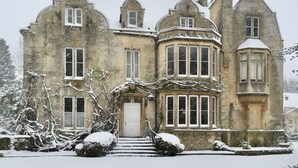 A historic stone building with a symmetrical facade, large windows, and a prominent bay window.