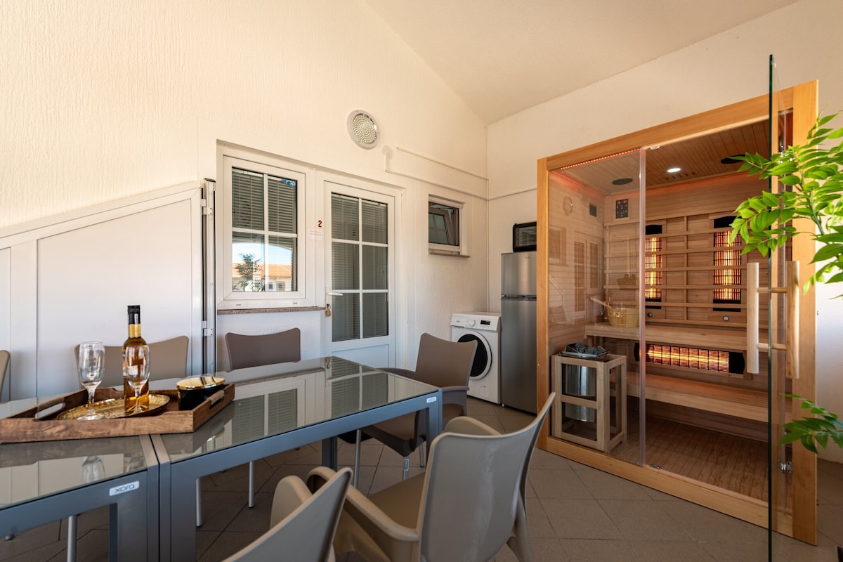 A modern kitchen with a glass dining table, a washing machine, and a sauna visible through a glass door.