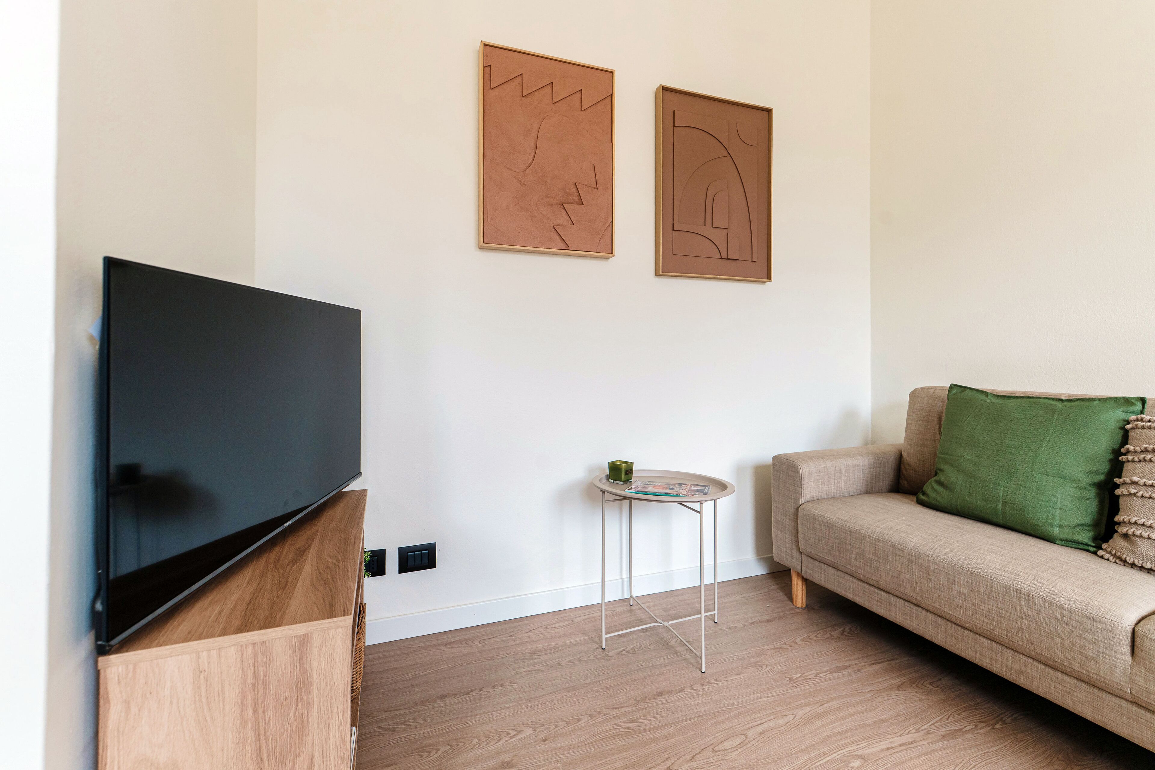 A modern living room with a flat-screen TV, a small round table, and a sofa with a green pillow.