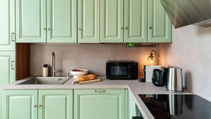 Une cuisine avec des meubles de rangement verts, un évier, un four à micro-ondes, un grille-pain et une bouilloire.