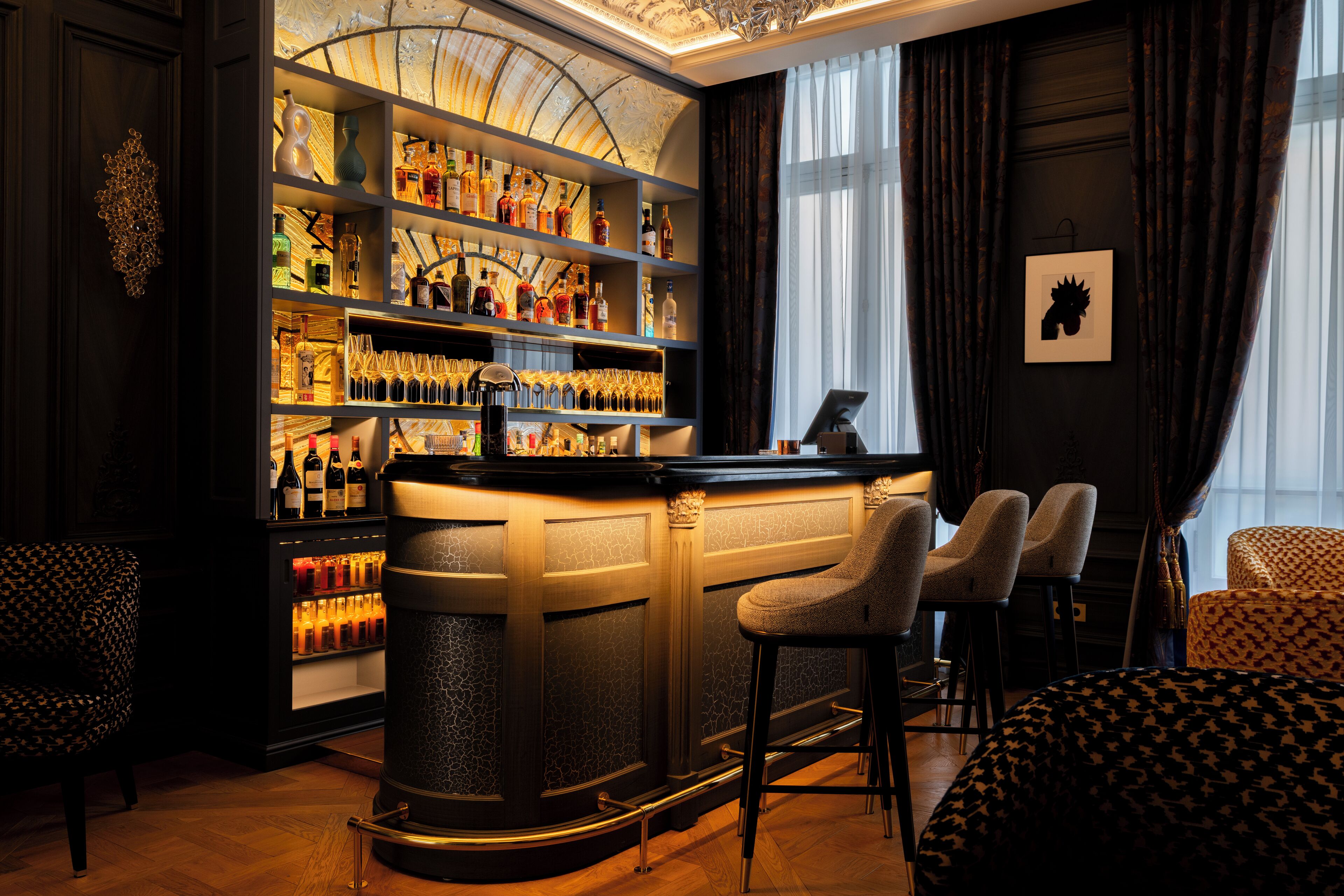 Zona de bar con estantes llenos de botellas de licor, una barra y dos taburetes.