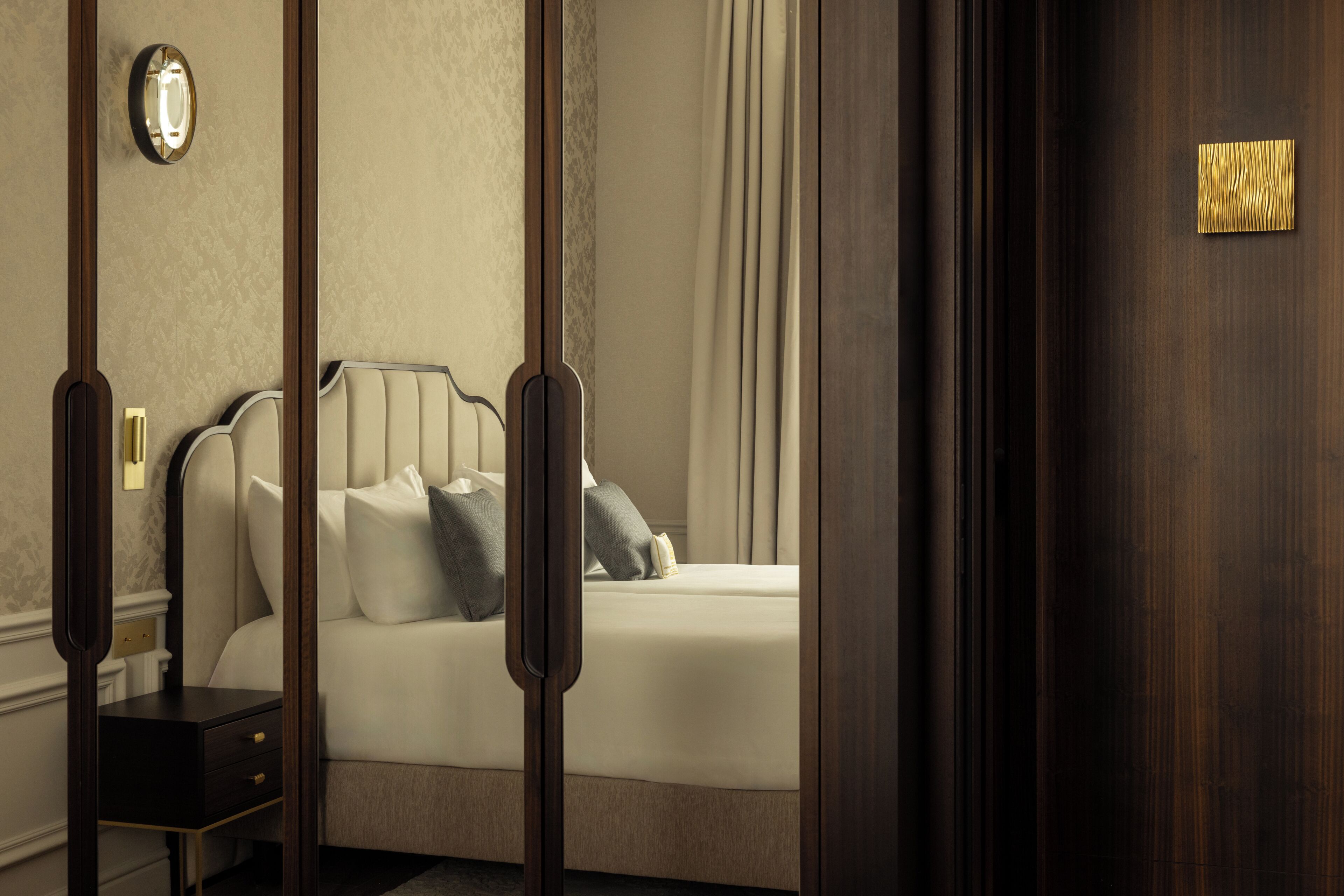 Een hotelkamer met een bed, nachtkastje, een wandklok en een deur met een gouden handgreep.