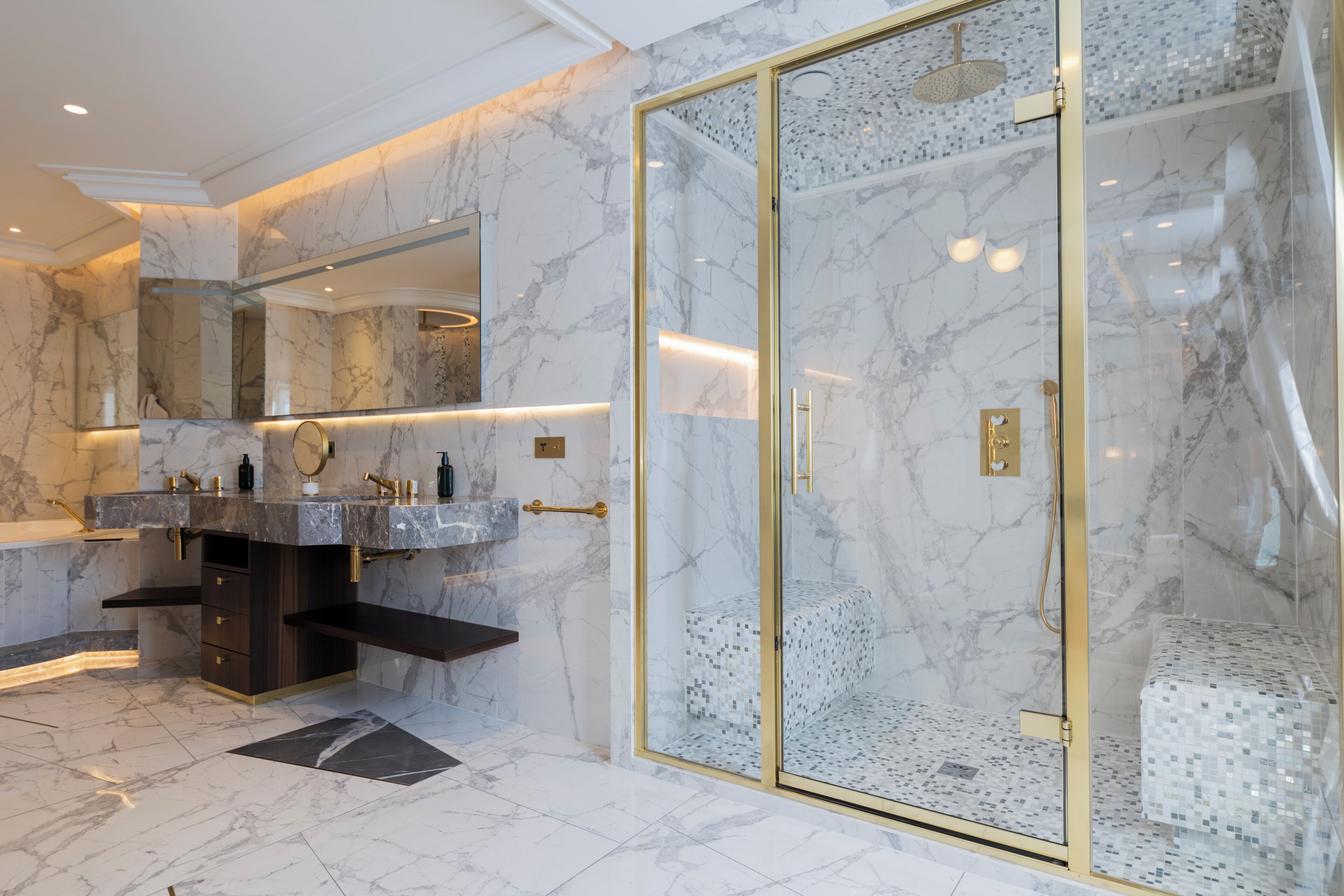 Un baño moderno con paredes de mármol, ducha con cerramiento de vidrio y tocador con doble lavabo.