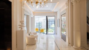 A spacious lobby with a chandelier, white columns, and a glass door leading to an outdoor area. - Maison Bauchart (Paris)