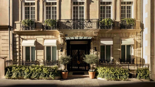 A multi-story building with a classical facade, multiple balconies with potted plants, and a central entrance with a decorative archway. - Maison Bauchart (Paris)