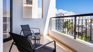 Un balcone con due sedie nere, un tavolino e un bicchiere d'acqua.