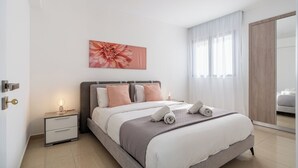 A modern bedroom with a large bed, a nightstand, a wall-mounted artwork, and a sliding door to a bathroom. - Averna - Breezy 2-BR Apt. in Larnaca (Larnaca)