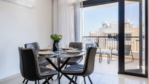 Un'area pranzo con un tavolo apparecchiato per quattro persone, sedie, un vaso con fiori e vista sulla città attraverso una porta in vetro.