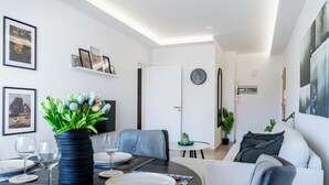 A modern living room with a dining area, featuring a round table, chairs, a sofa, and a TV. - Averna - Breezy 2-BR Apt. in Larnaca (Larnaca)