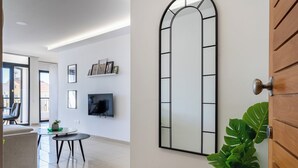 A modern living room with a large mirror, a flat-screen TV, and a dining area with a table and chairs. - Averna - Breezy 2-BR Apt. in Larnaca (Larnaca)