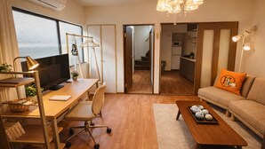 Un salon moderne avec un bureau en bois, un canapé confortable, une table basse et une cuisine en arrière-plan.