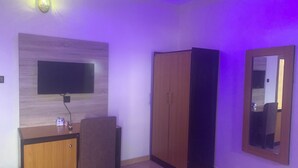 Een kamer met een houten bureau, een stoel, een kledingkast, een aan de muur bevestigde televisie en een spiegel.