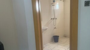 A bathroom with a shower, sink, and a blue trash bin.