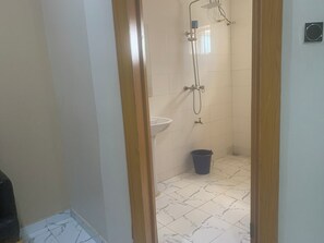 A bathroom with a shower, sink, and a blue trash bin. - Comfort Kul Suites (Agbor)