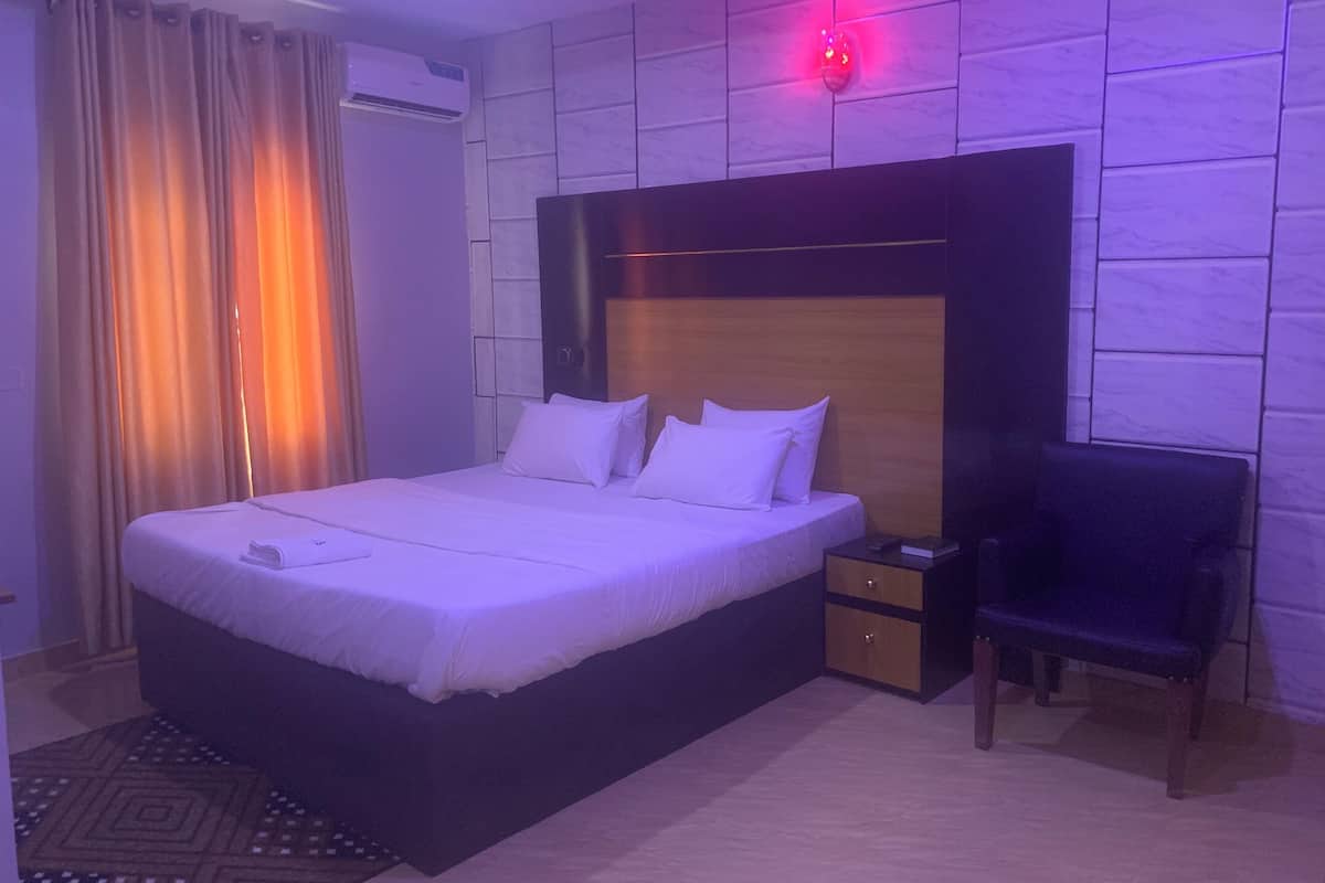 Ein Hotelzimmer mit Bett, Nachttisch, Stuhl und Wandklimaanlage.