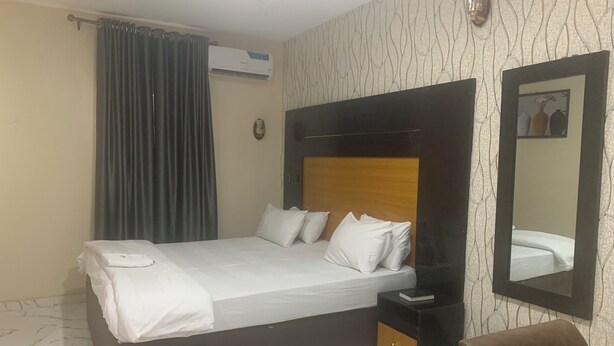 Een hotelkamer met een bed, nachtkastje, spiegel en gordijn.
