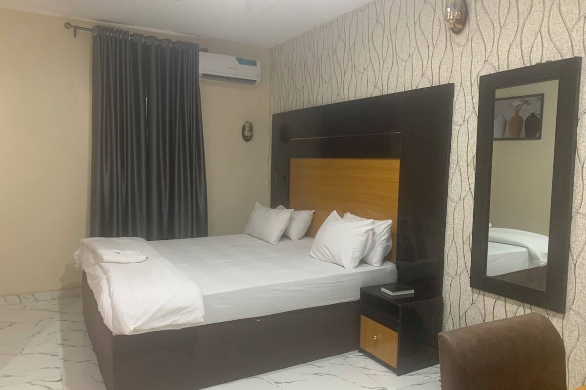 Ein Hotelzimmer mit Bett, Nachttisch, Spiegel und Vorhang.