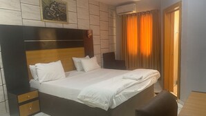 A bedroom with a large bed, a nightstand, a chair, a wall-mounted air conditioner, and a door.