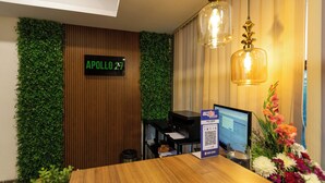 Ein Empfangsschalter mit Holzoptik, eine digitale Anzeige mit der Aufschrift "APOLLO 27", ein Computermonitor und ein QR-Code auf einer Karte.