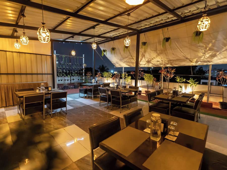 An outdoor dining area with tables and chairs, hanging lights, and potted plants.