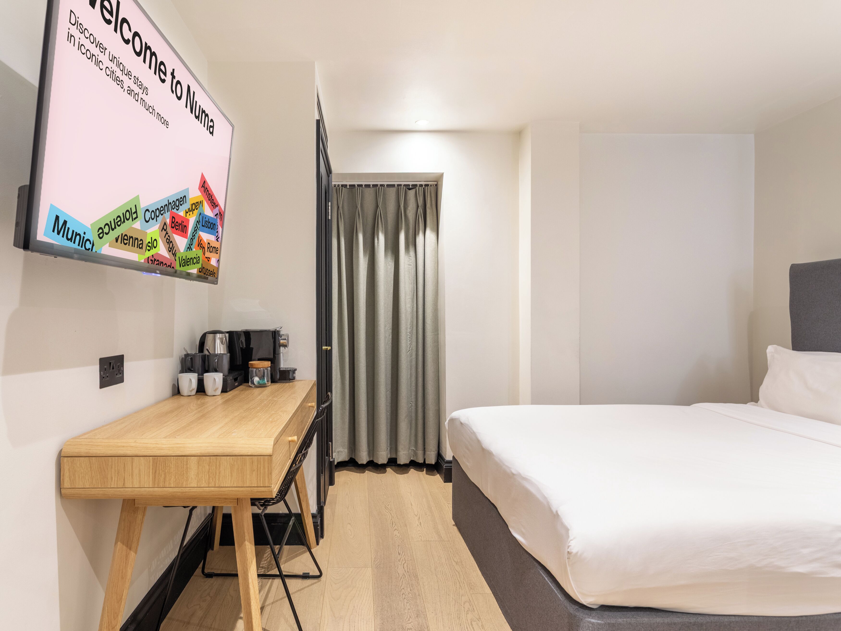 A hotel room with a wooden desk, a bed, and a TV displaying a welcome message.