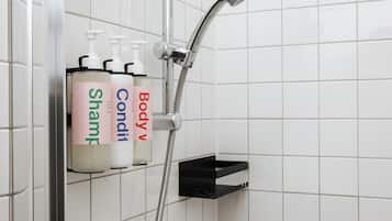 A bathroom with a shower, a black shelf, and three bottles of shampoo labeled 'Shampoo,' 'Condition,' and 'Body V.'
