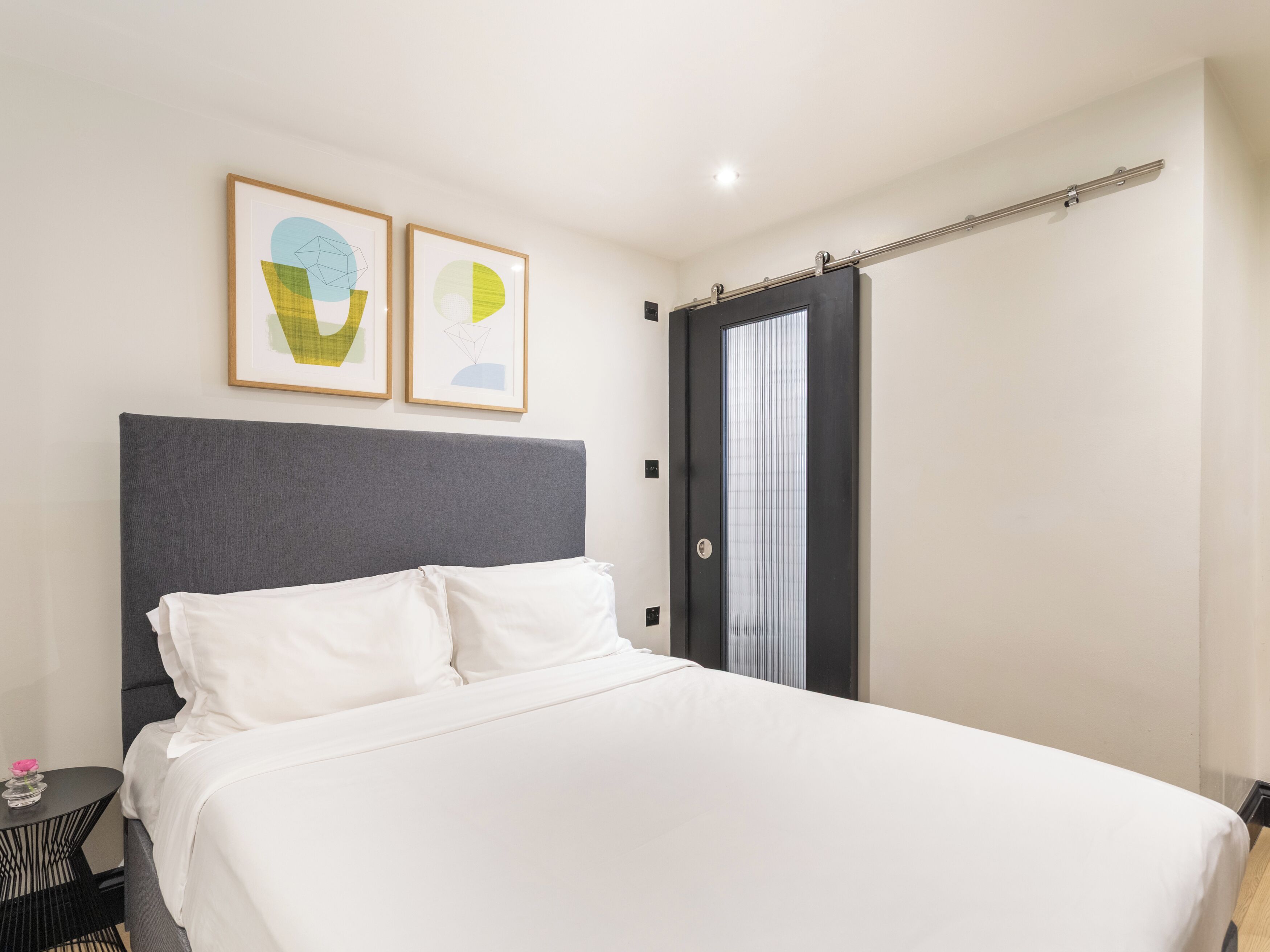 A modern hotel room with a large bed, a grey headboard, and two abstract paintings on the wall.