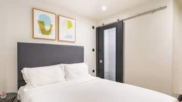 A modern hotel room with a large bed, a grey headboard, and two abstract paintings on the wall.