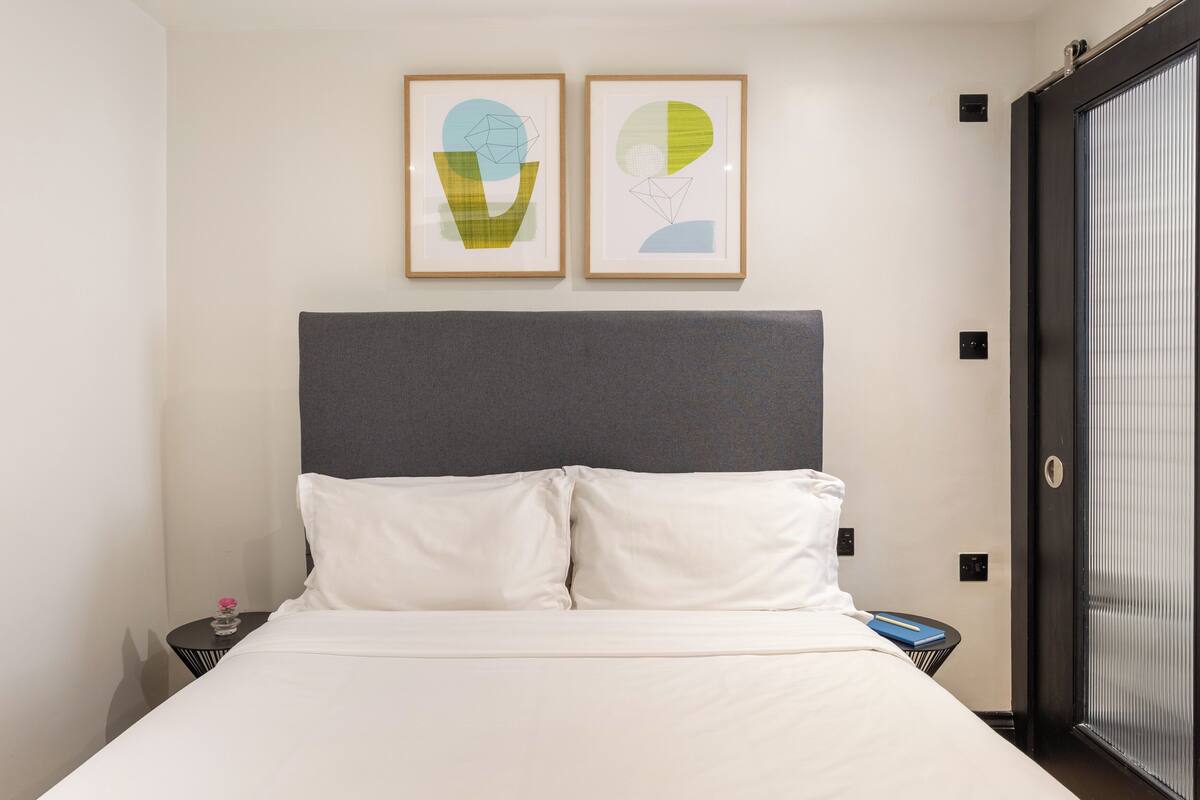 Een hotelkamer met een bed, twee ingelijste abstracte kunstwerken, een grijze hoofdeinde en een deur met een handgreep.
