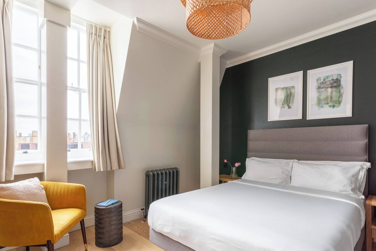 Een slaapkamer met een bed, een stoel, een radiator en kunst aan de muur.