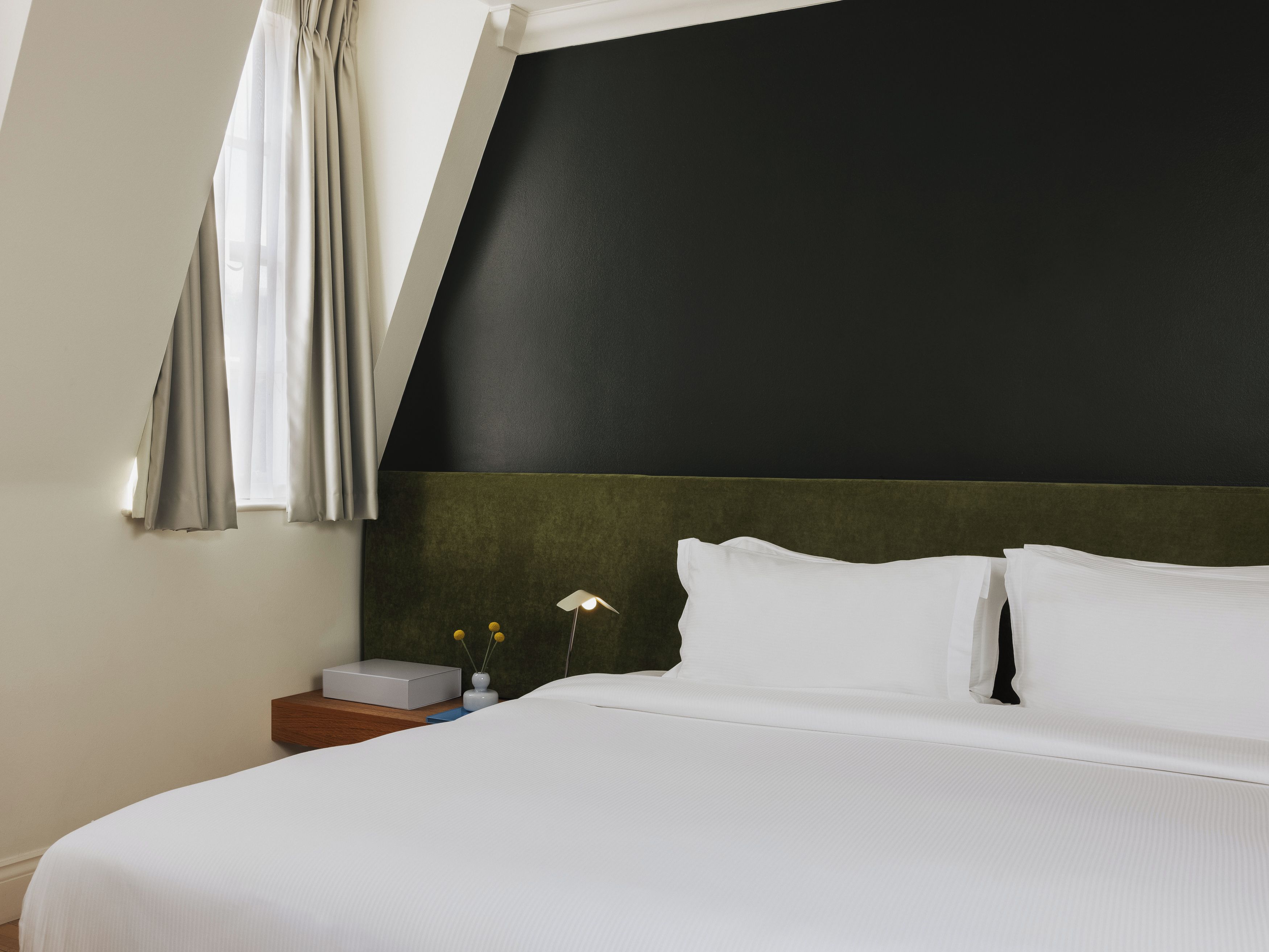 A hotel room with a bed, a nightstand, a lamp, and a window with curtains.