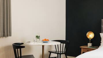 A hotel room with a round table, two chairs, a bedside table with a lamp, and a bed.