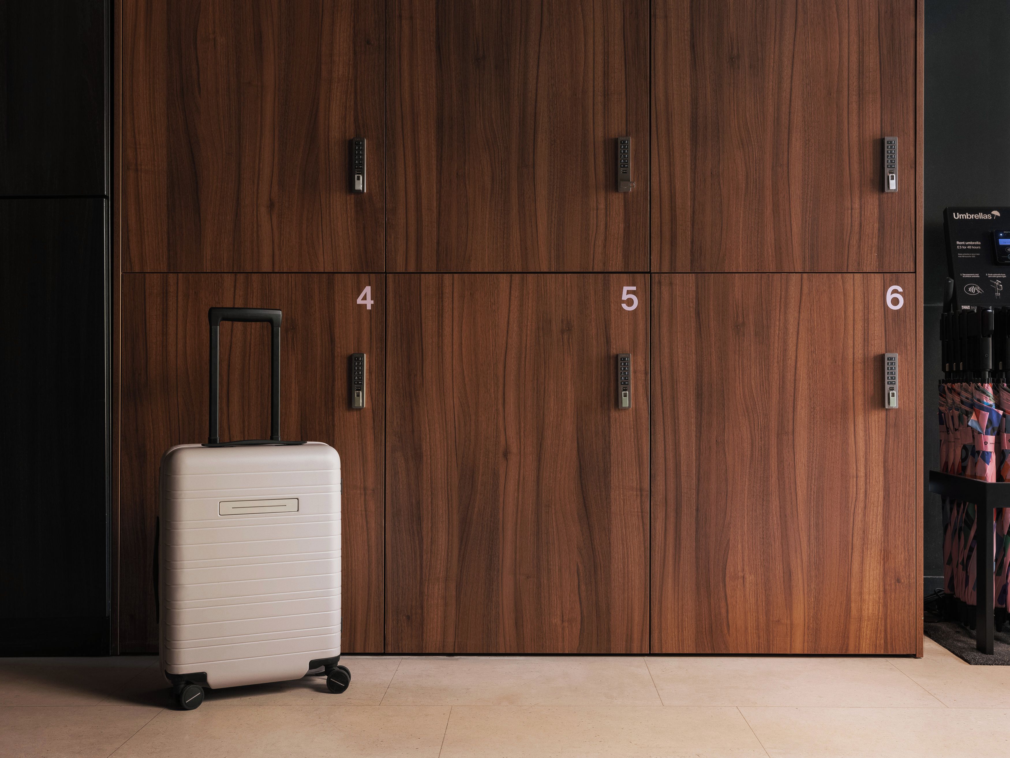 Una habitació amb un armari de fusta, portes numerades, una maleta i un suport amb ombrelles.