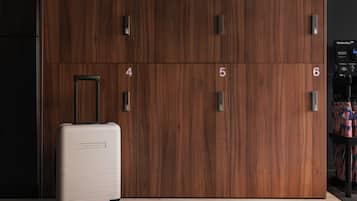 Una habitació amb un armari de fusta, portes numerades, una maleta i un suport amb ombrelles.