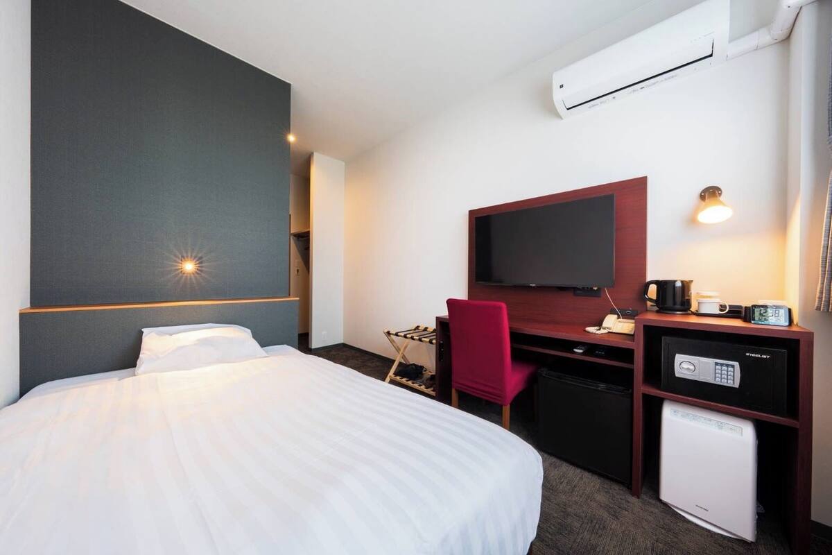Una camera d'albergo con un letto, una scrivania con televisore, un forno a microonde e un mini frigorifero.