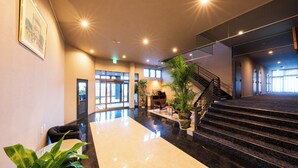 A spacious lobby with a marble reception desk, a staircase, and a large potted plant. - SPACEPORT HOTEL OITA (Kunisaki)