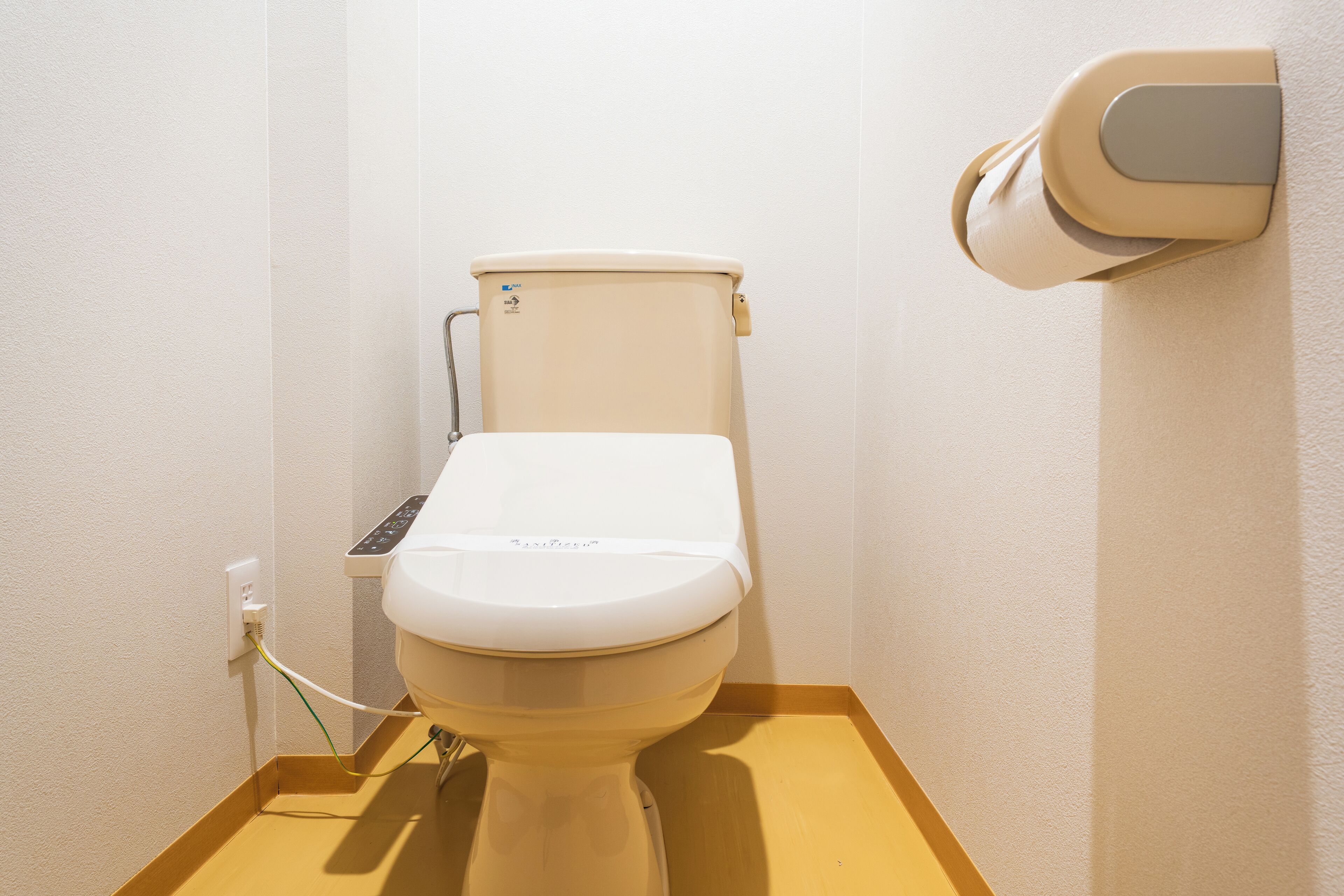 A toilet with a control panel, a wall-mounted toilet paper holder, and a power outlet.