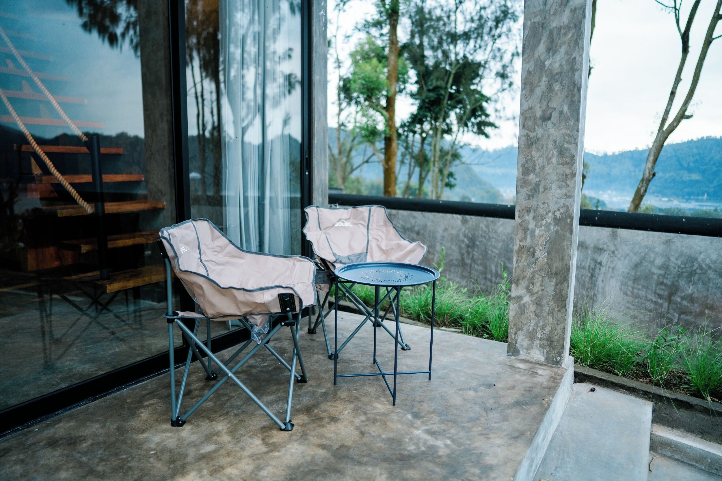 Un patio con dos sillones plegables y una mesita redonda, con vistas a un paisaje con árboles y colinas.