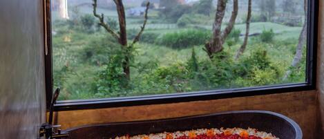A bathtub filled with red and orange flowers, a window with a view of a green landscape, and a wooden ceiling.