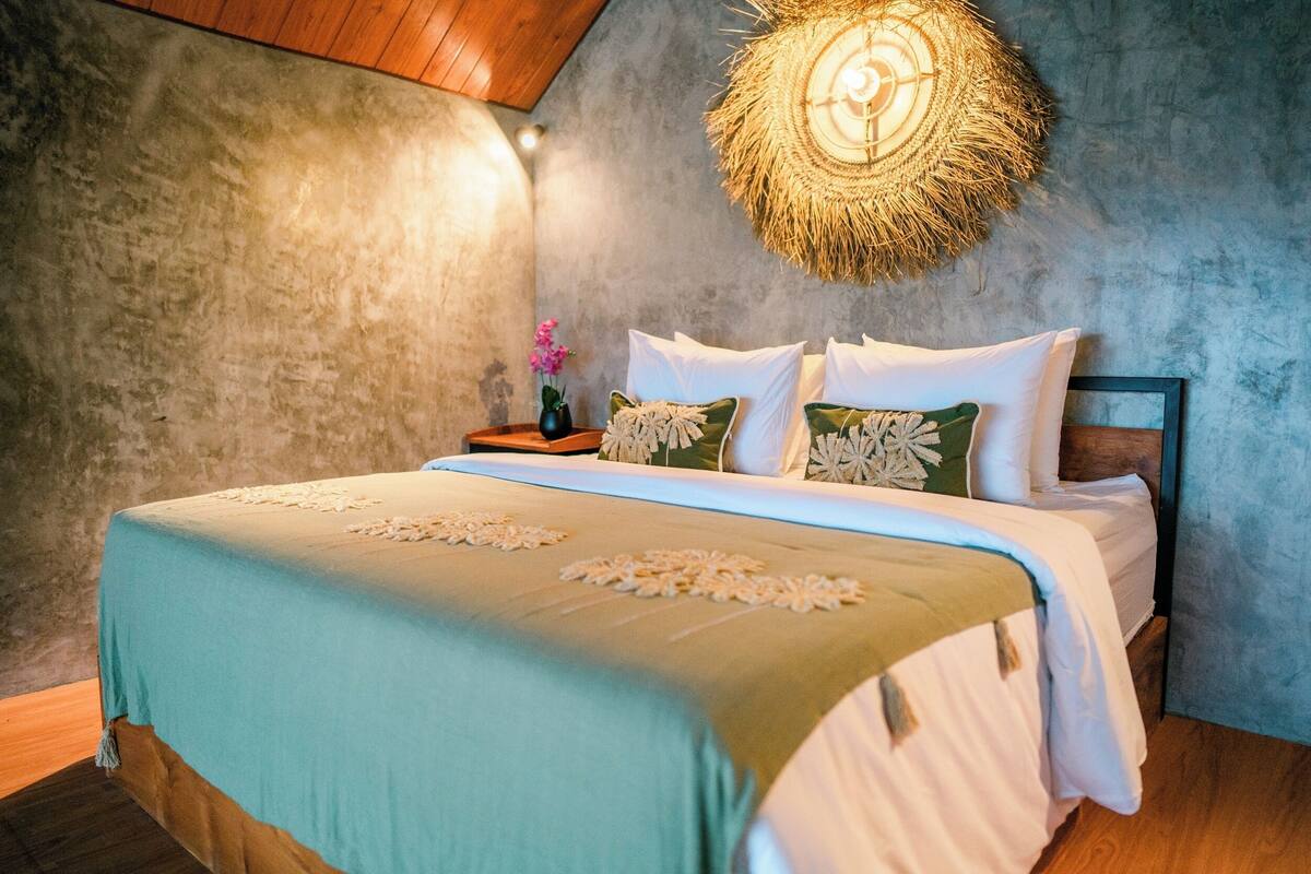 Una camera da letto con un letto, cuscini, un comodino e una lampada a muro.
