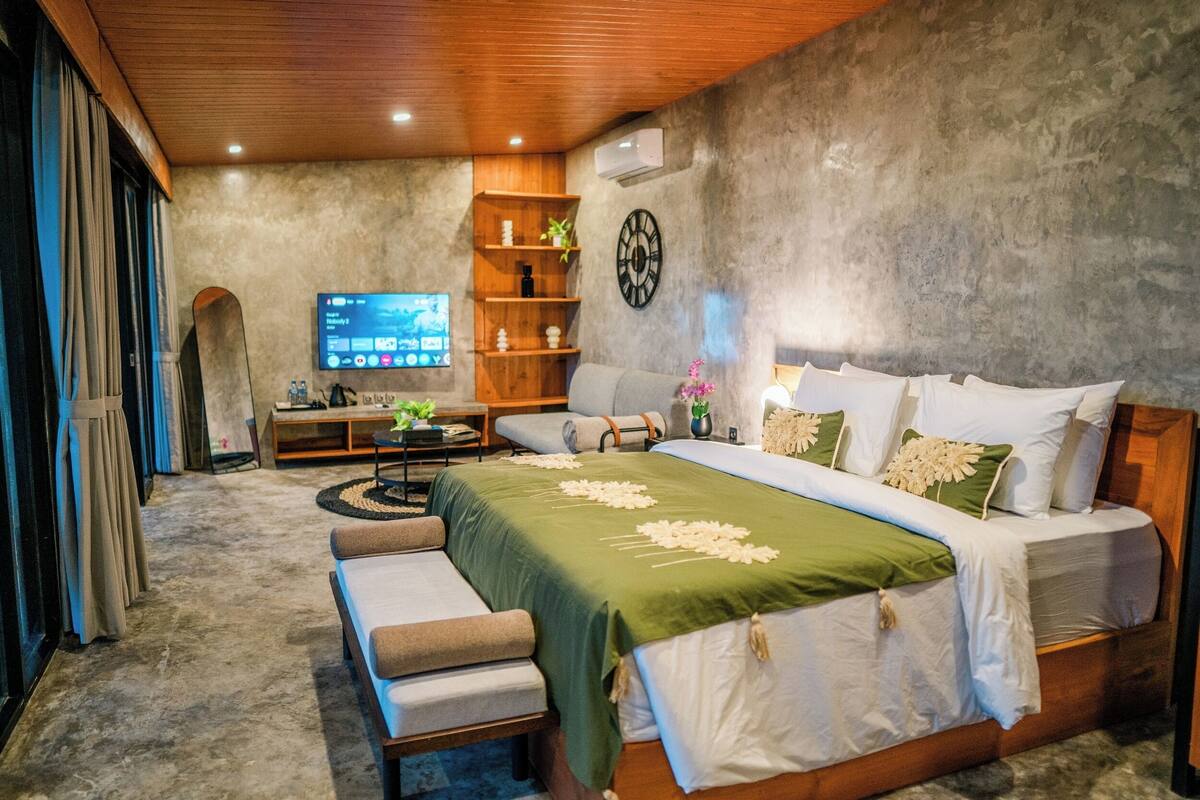 Una camera da letto moderna con un letto grande, una panca in legno, una TV e una mensola con oggetti decorativi.